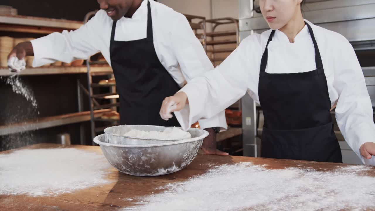 Happy diverse bakers working in bakery kitchen, pouring flour on counter in slow motion