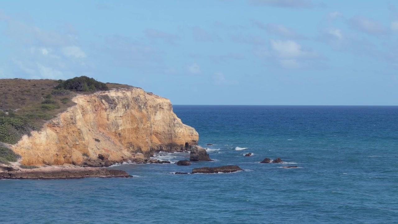 Imagem aérea de drone de um alto penhasco costeiro e praia de areia ao longo da água azul-turquesa do oceano no Porto Rico tropical sob um céu limpo