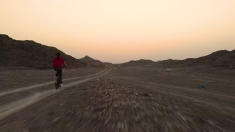 young teenager riding a folding bike in a flat off road terrain by the mountains in fujairah, united arab emirates