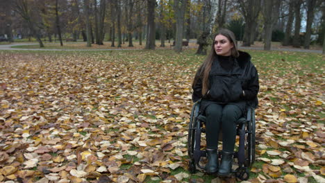 auténtica mujer discapacitada que sufre de pérdida de masa muscular sentada en silla de ruedas y relajándose en el parque de otoño