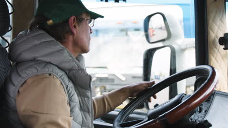 close up view of older worker wearing cap and vest driving a truck in a logistics park 1