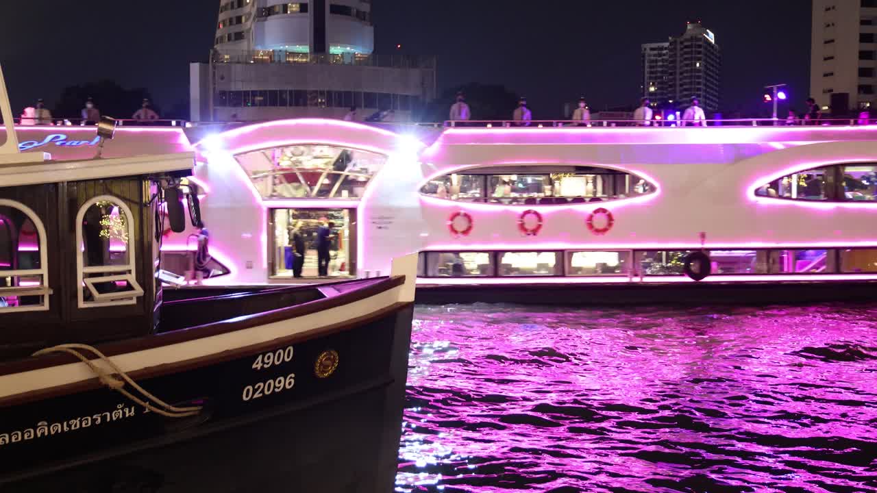 un barco brillantemente iluminado navega por un río por la noche.