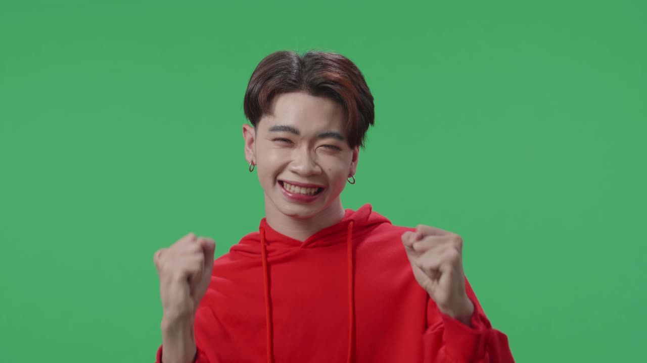 Cheerful Young Asian Transgender Male Celebrating While Standing On Green Screen In The Studio