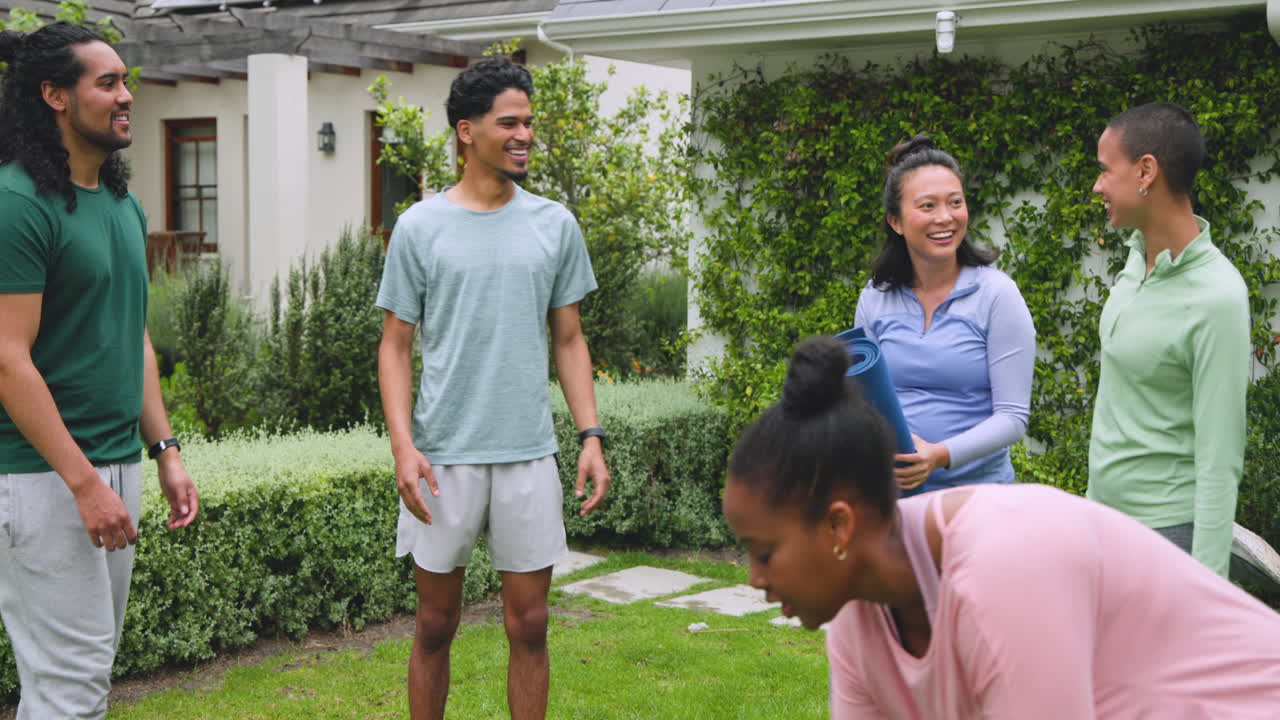 diverse friends laughing and preparing for outdoor yoga session with mats in garden