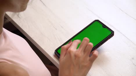 una chica durante una manicura usa un teléfono inteligente con una pantalla verde. servicio de manicura hecho a sí mismo. la manicurista pinta las uñas con gel polaco rosado. uñas rojas manicuradas. aplicación de esmalte de uñas.
