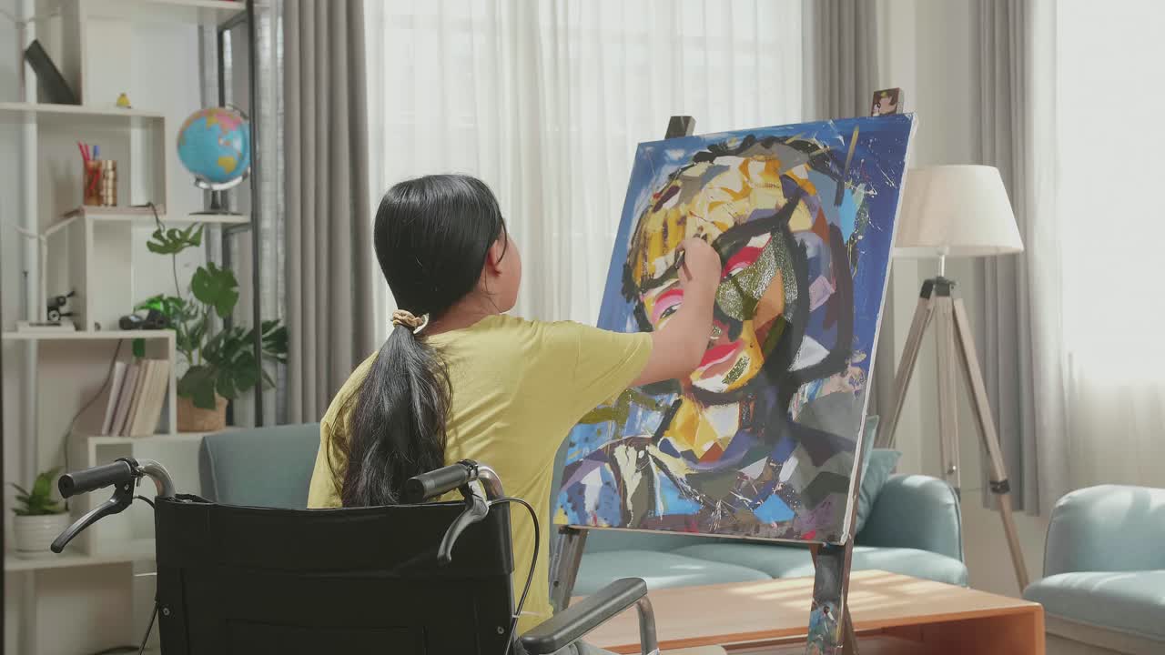 Hind View Of An Asian Artist Girl In Wheelchair Thinking And Painting A Girl'S Face On The Canvas