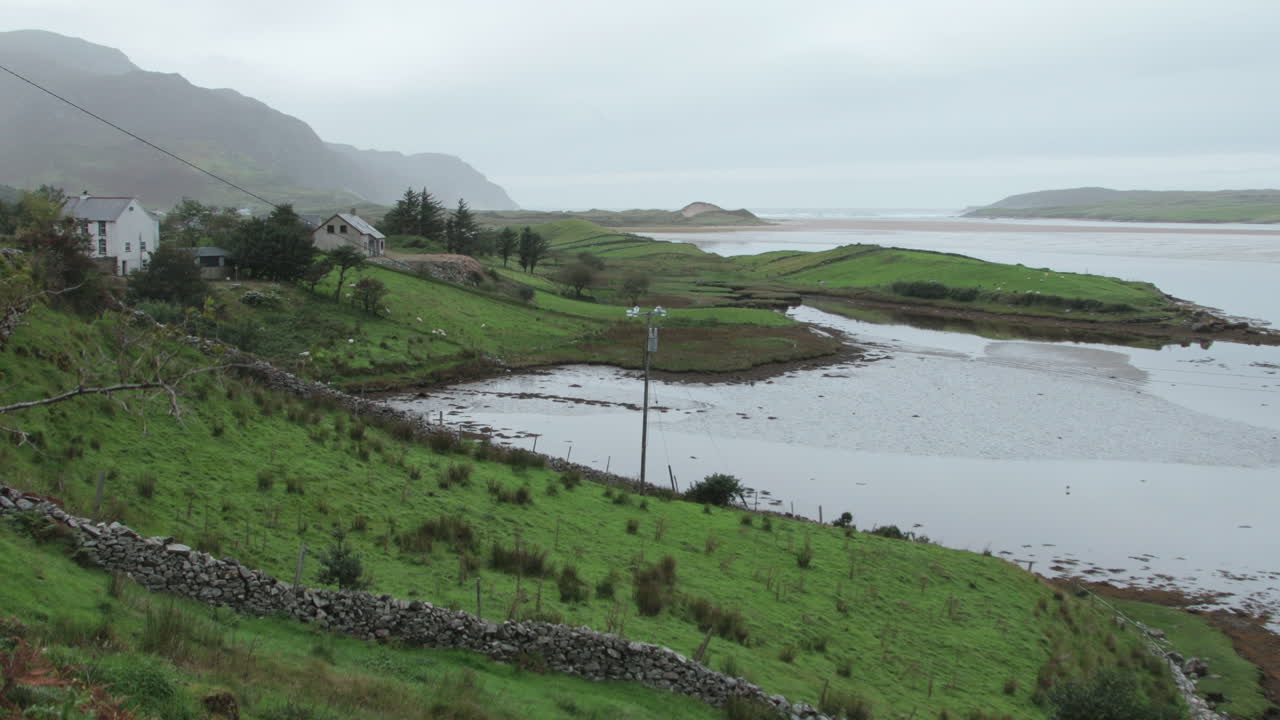 A tranquil view captures the lush green hillsides and calm waters of County Donegal in North East Ireland, framed by distant hills and an overcast sky.