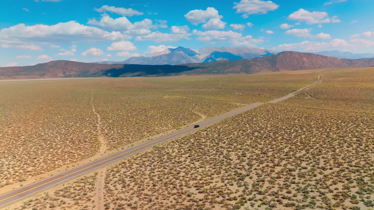 Motorway along the desert limited by mountain range. Soft cumulus clouds throwing shadows on the rocks. Aerial view.