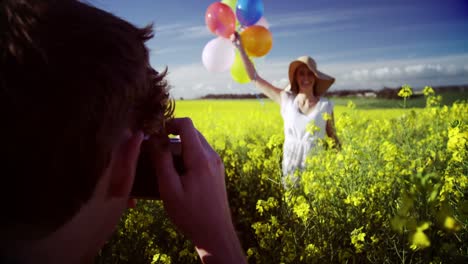 Man-photographing-woman-with-balloons-in-mustard-field