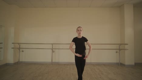 a group of young ballet students in black dancewear practicing positions in a spacious ballet studio with wooden flooring and wall-mounted barres. focused expressions and synchronized movements.