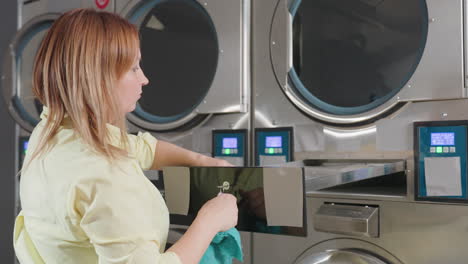 manager returns cleaned lint filter into drawer of industrial washer, guiding mesh panel with turquoise towel, routine maintenance inside laundromat, stainless units lined in row, hygiene focus