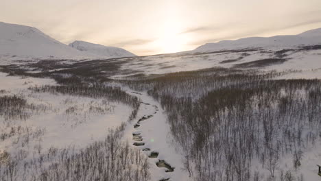 Cabin-on-frozen-river-bank-in-remote-wilderness-of-snowy-landscape