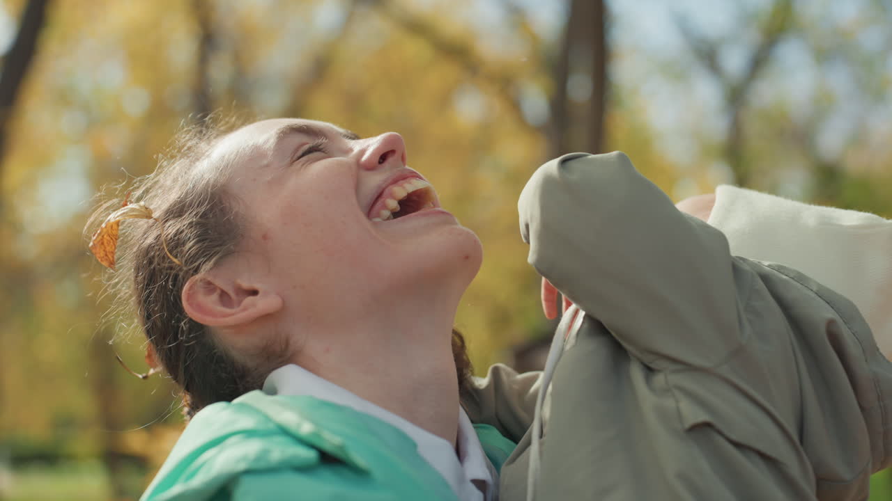 Eine Mutter lacht mit ihrem Kleinkind im Park. Goldene Blätter und Sonnenlicht, offenes Lächeln und freudige Gesten. Eine enge Umarmung und Strickmütze. Eine herzliche Familienbindung, eingefangen in aufrichtigen Emotionen.