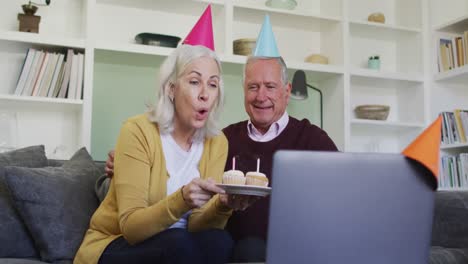 happy senior caucasian couple celebrating a birthday making video call using laptop computer