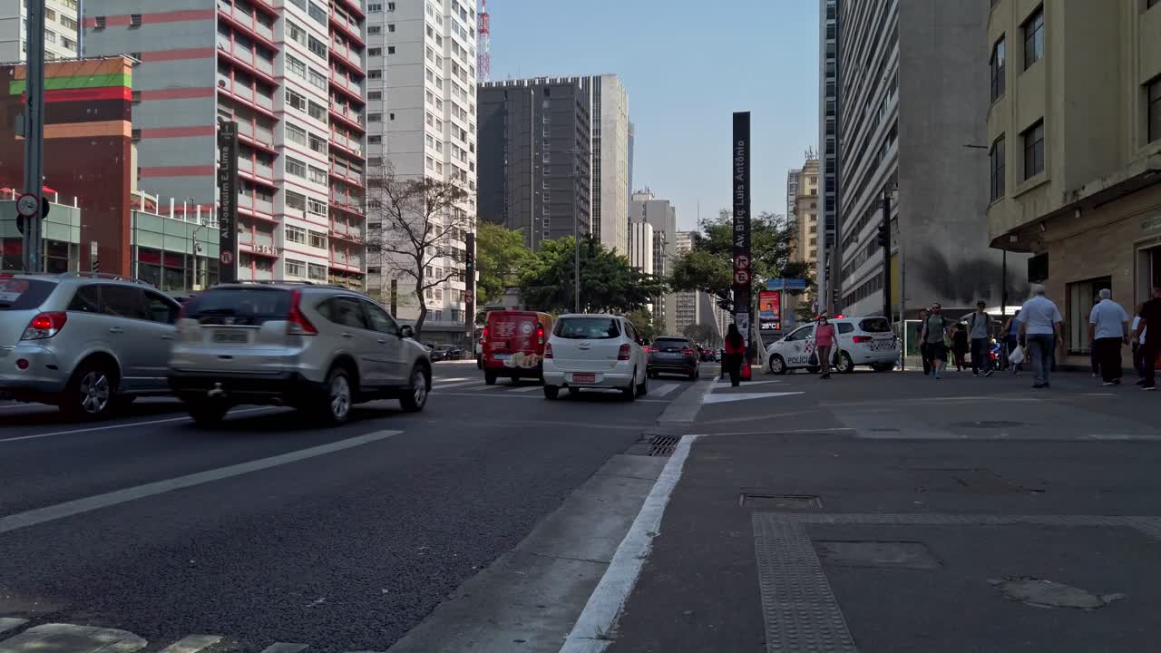 Vehicles maneuver through bustling streets in the financial district as pedestrians navigate the sidewalks in the warm afternoon sun