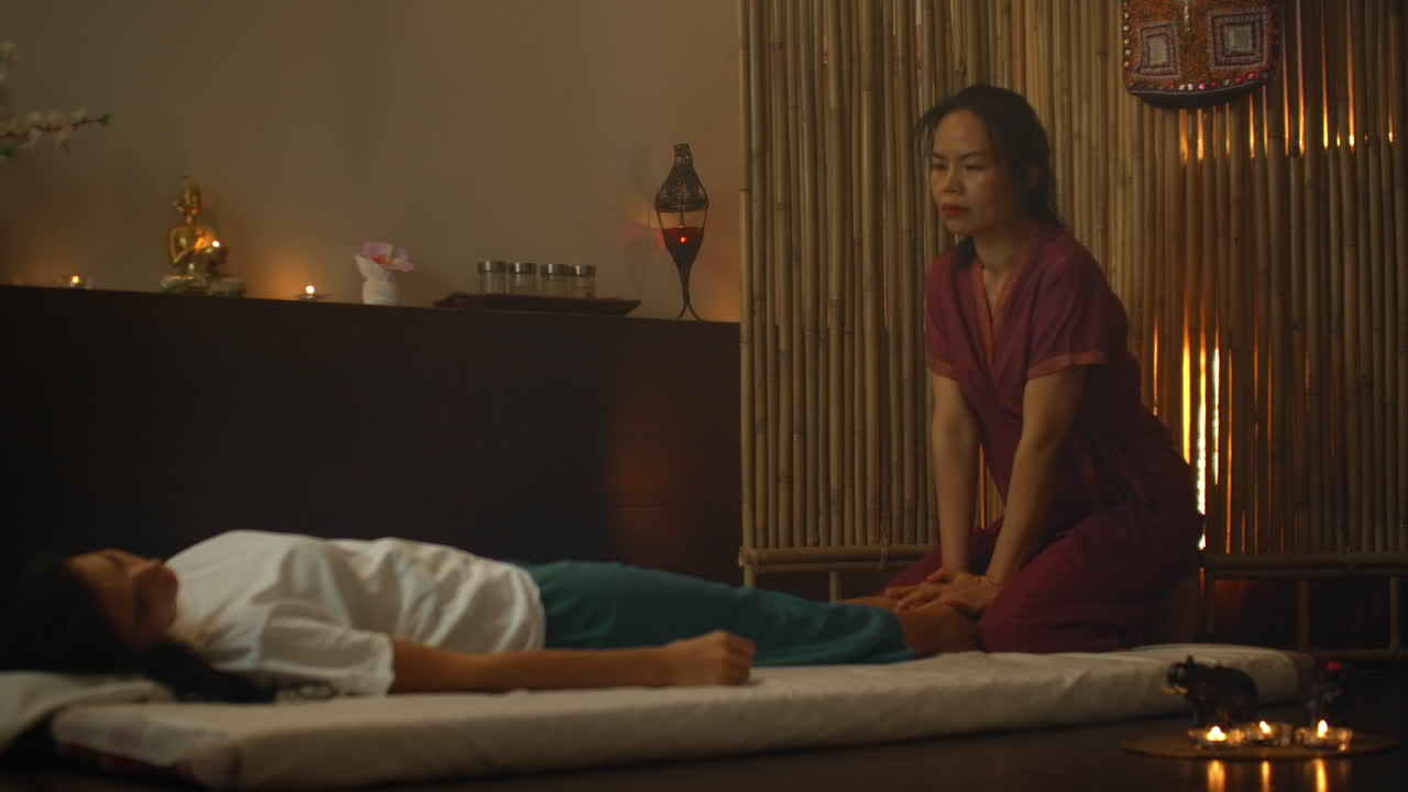 An Asian woman performs a traditional Thai massage on the back of a lying beautiful European girl. Chiropractor produces treatment with alternative methods.