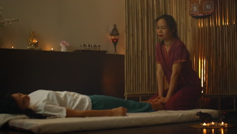 an asian woman performs a traditional thai massage on the back of a lying beautiful european girl. chiropractor produces treatment with alternative methods.