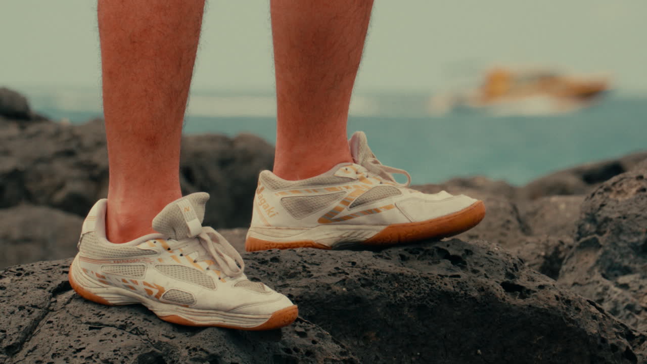 Person wearing sneakers on rocks near the ocean