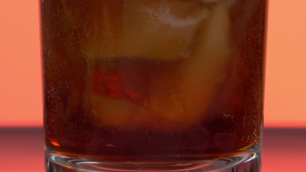 un primer plano de refresco oscuro gaseoso con cubos de hielo en un vaso, fondo naranja