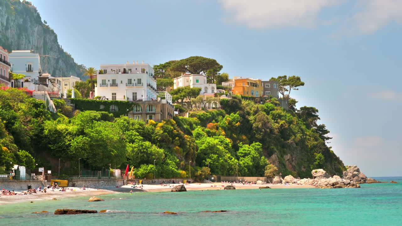 Vista della costa tirrenica a Capri, Italia. Edifici classici, spiaggia con persone che si rilassano, vegetazione.