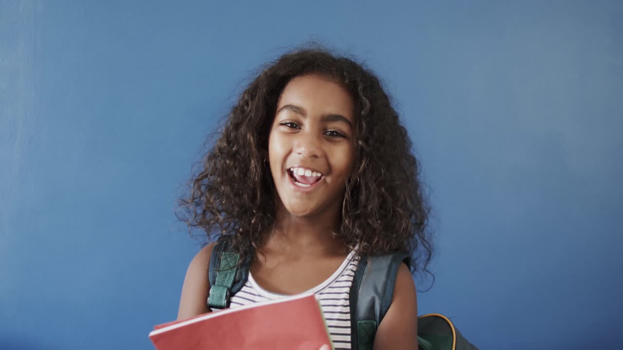 Portrait of happy african american girl holding books on blue background, slow motion