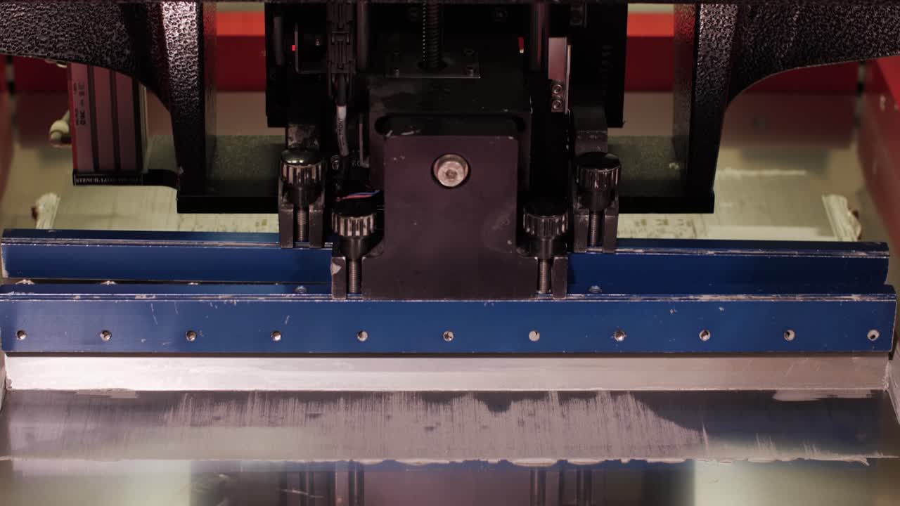Close-up of an applicator spreading material on a perforated surface in an automated manufacturing process