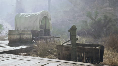 old west water pump and covered wagon in a desolate desert landscape