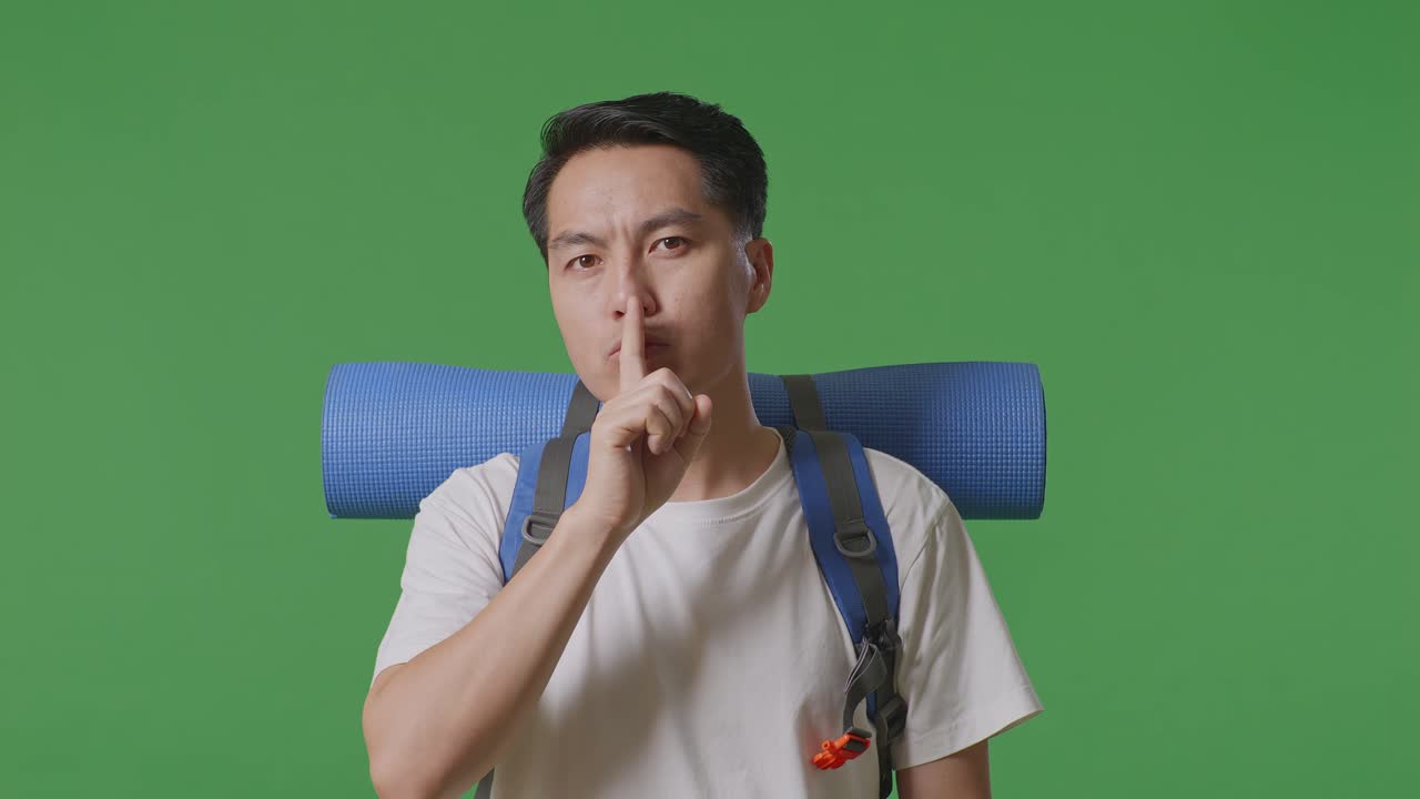 Man with a backpack making a shhh gesture