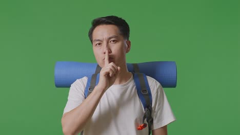 man with a backpack making a shhh gesture