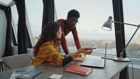 multiethnic colleagues discussing project on laptop in rooftop office