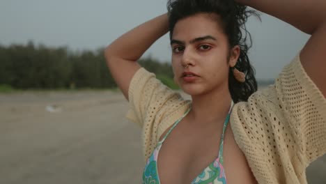 Woman-adjusting-hair-on-beach-at-dusk,-close-up-of-face-with-a-serene-expression,-soft-focus-on-background