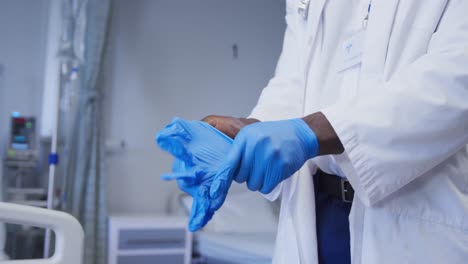 Mittelteil-Eines-Afroamerikanischen-Männlichen-Arztes,-Der-Latexhandschuhe-Im-Patientenzimmer-Des-Krankenhauses-Trägt