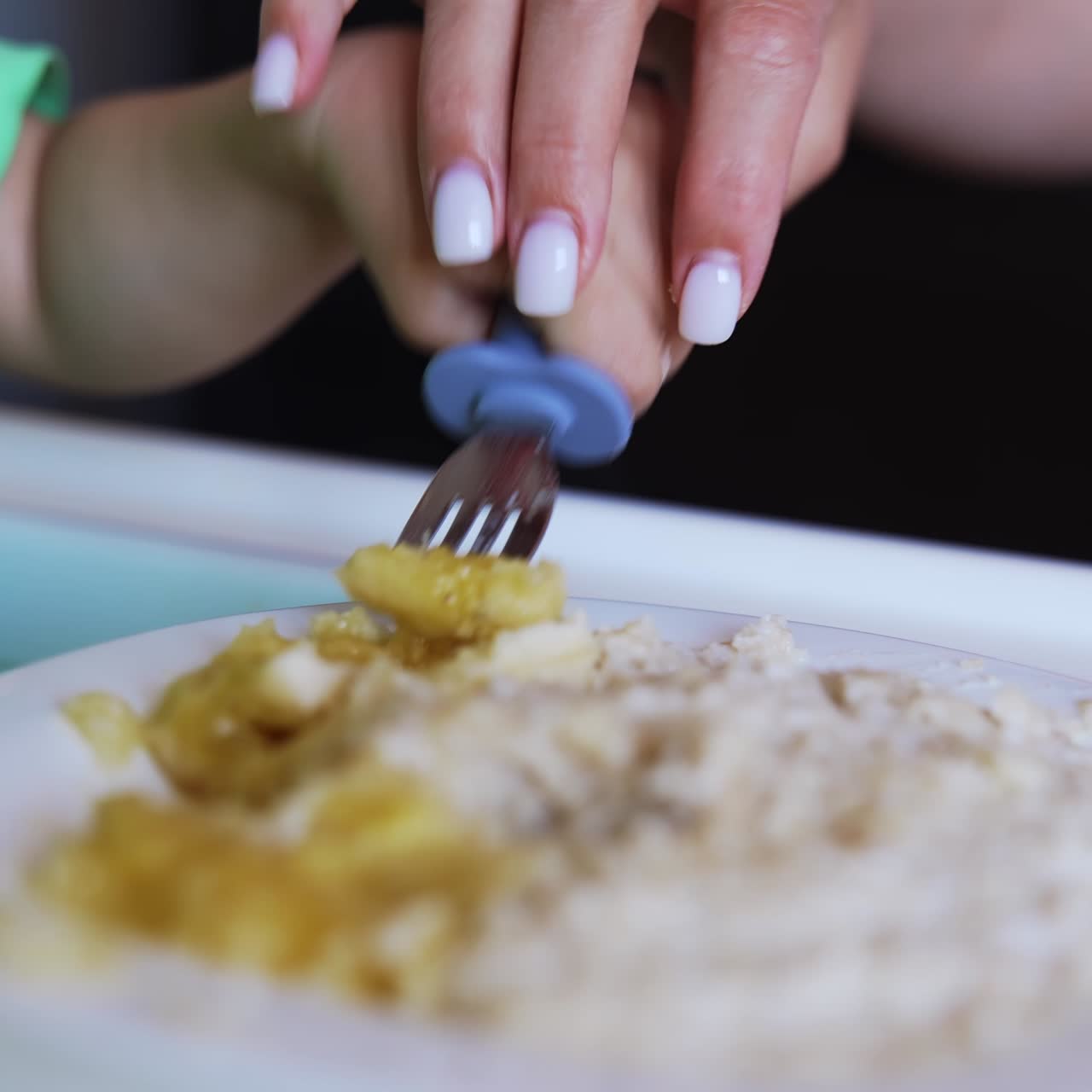 Cute baby boy wearing green t-shirt eating from fork. Mom helps her son to pick up the food. Close up