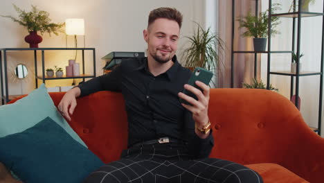portrait of adult man sitting on sofa, using smartphone share messages on social media application