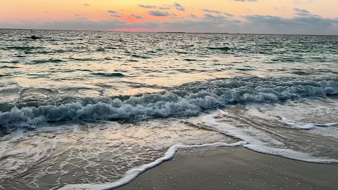Slow motion di onde oceaniche che si infrangono sulla riva durante un tramonto vibrante.