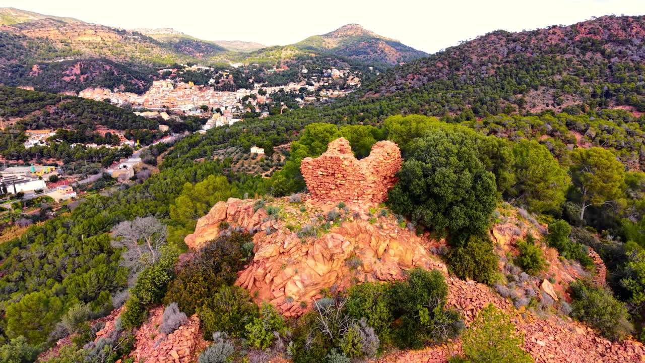 Resti di un'antica struttura di fortificazione in pietra situata su un picco aspro che domina una valle verde e montagne lontane. Ruderi di un'antica torre in pietra in cima a una collina rocciosa rossa.