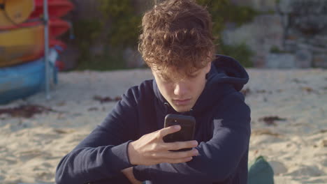 teenage boy texts on smartphone on beach, portrait