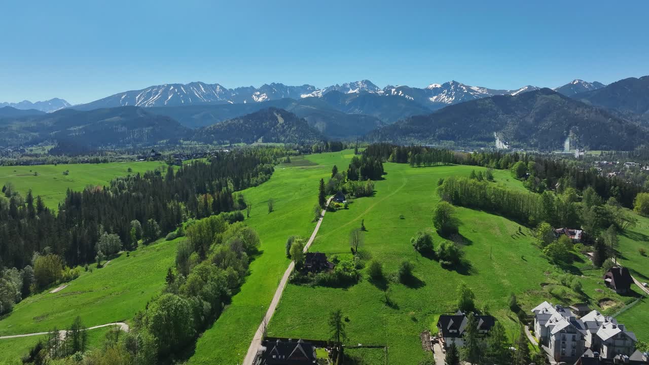 Aerial View of a Scenic Mountain Valley with Green Fields and Snow-Capped Peaks