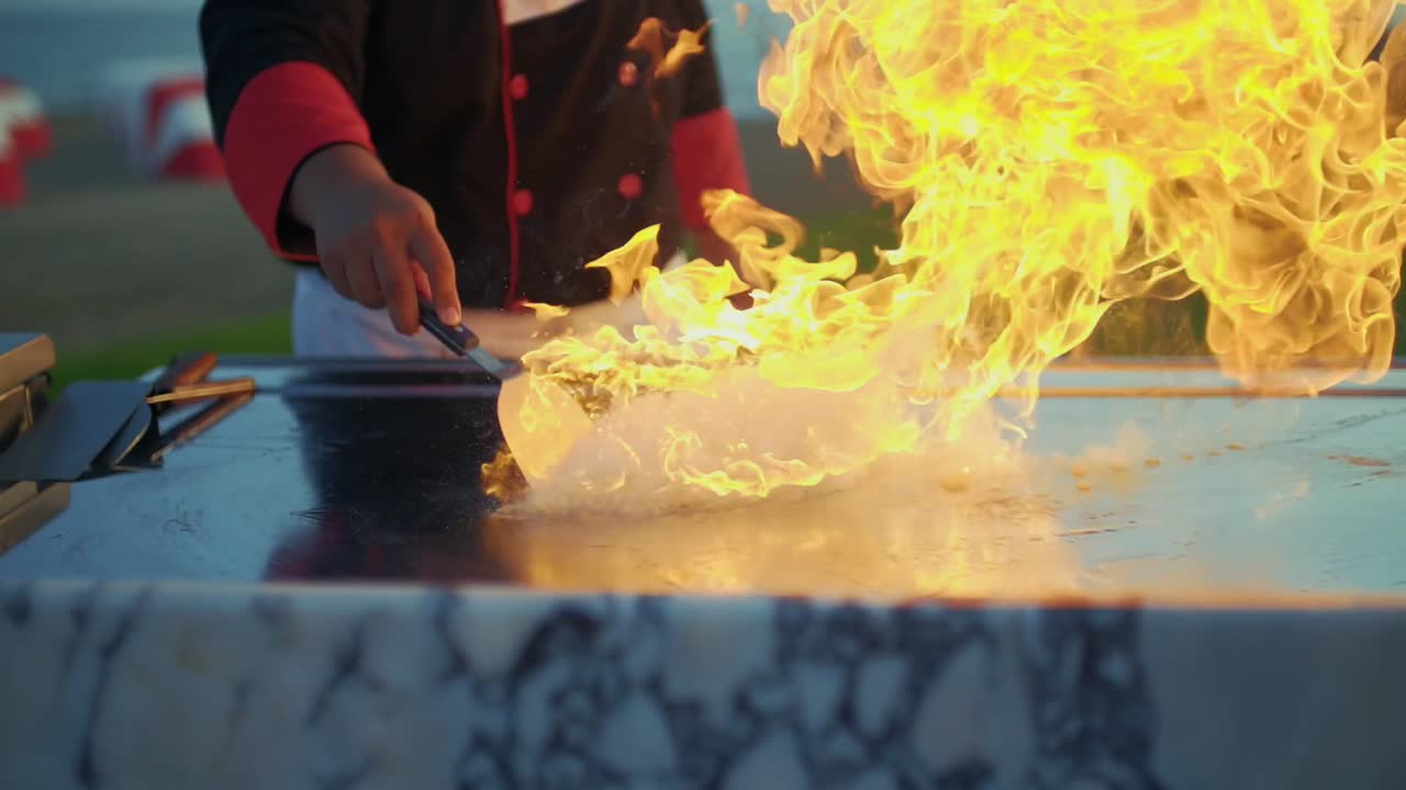 The cook pours oil on the grill with the art of teppanyaki. and flames come out.