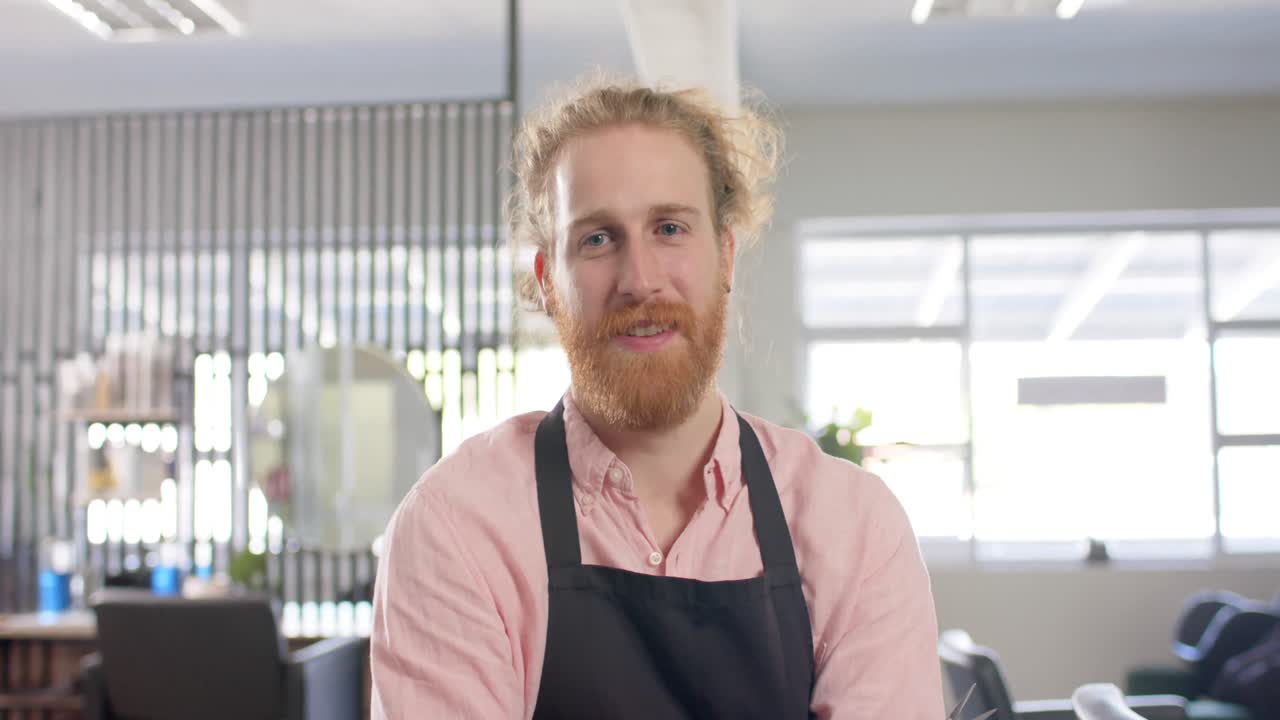 retrato de un peluquero caucásico barbudo en delantal sonriendo en el salón de peluquería, cámara lenta