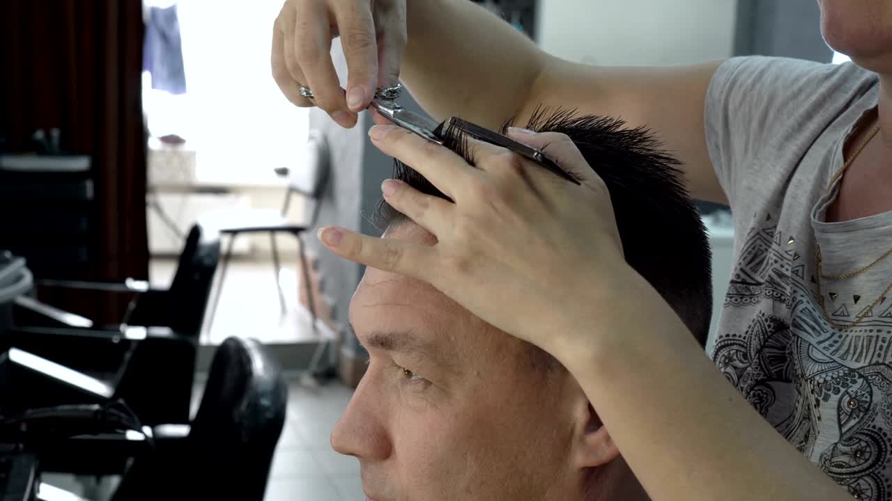mujer peluquera corta el cabello de un hombre en un salón de belleza. se peina el cabello con un peine y lo corta con tijeras. cuidado del cabello
