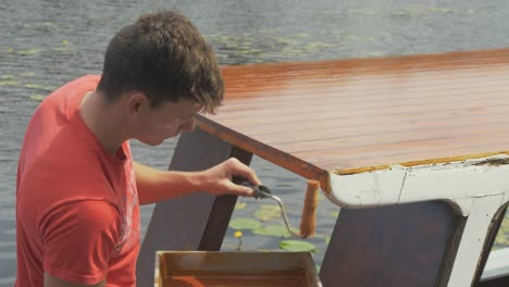 Young-carpenter-paints-edge-of-wooden-boat-cabin-with-roller