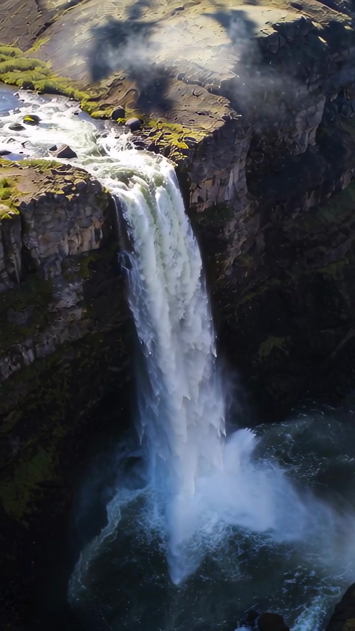 Video verticale: Raggiungendo il bordo di una scogliera, un fiume si riversa su un altopiano, la gravità lo trascina in una pozza d'acqua sottostante.