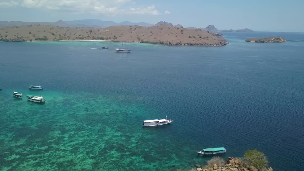 Tourist boats moored on Idyllic bay encircled by Pink Beach Komodo Island, Indonesia - Wide Aerial Panoramic shot