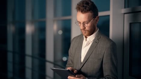 charismatic young businessman with tablet on night city background with office skyscraper
