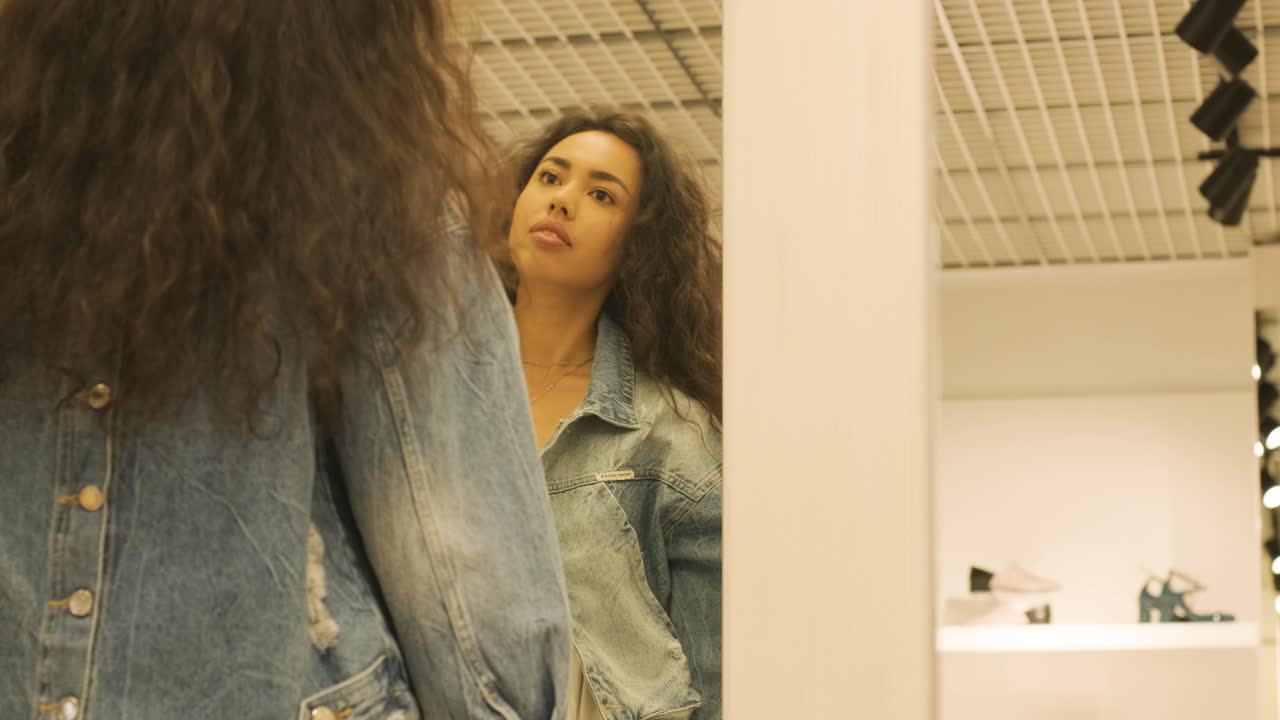una chica feliz y elegante probando un traje en el camerino de una tienda de ropa boutique de interiores con iluminación brillante.