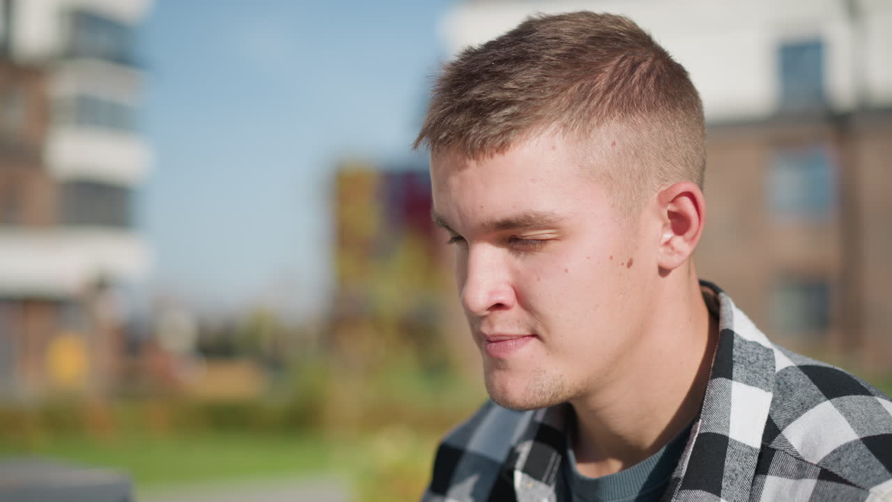 close up of white man closing eyes in calm expression while taking red pill medication for relief seated outdoors on wooden bench with urban buildings blurred in background