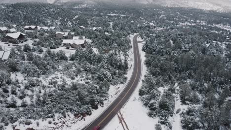 Vista-Aérea-De-Un-Auto-Rojo-Solo-Conduciendo-A-Través-De-Los-Bosques-Rurales-Cubiertos-De-Nieve-De-Arizona