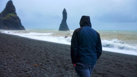 Vista-Trasera-De-Un-Turista-Masculino-Caminando-Solo-En-La-Playa-De-Arena-Negra-Reynifjara-En-Vik,-Islandia