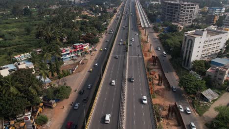 cinematic aerial footage reveals a service road, swiftly driving cars, and residential commercial buildings on an indian highway that is rapidly growing